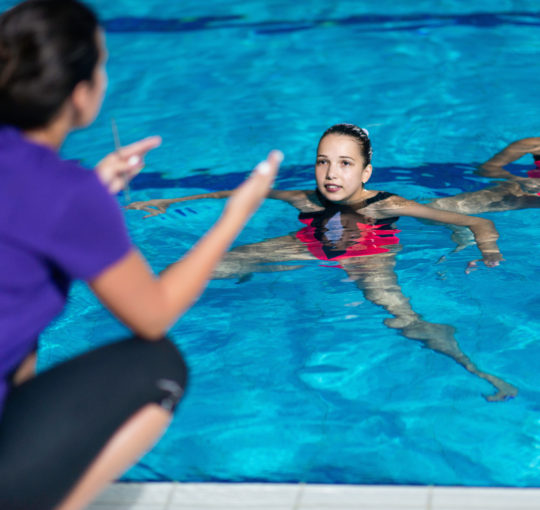 A coach gives instructions to his artistic swimmers in the pool.