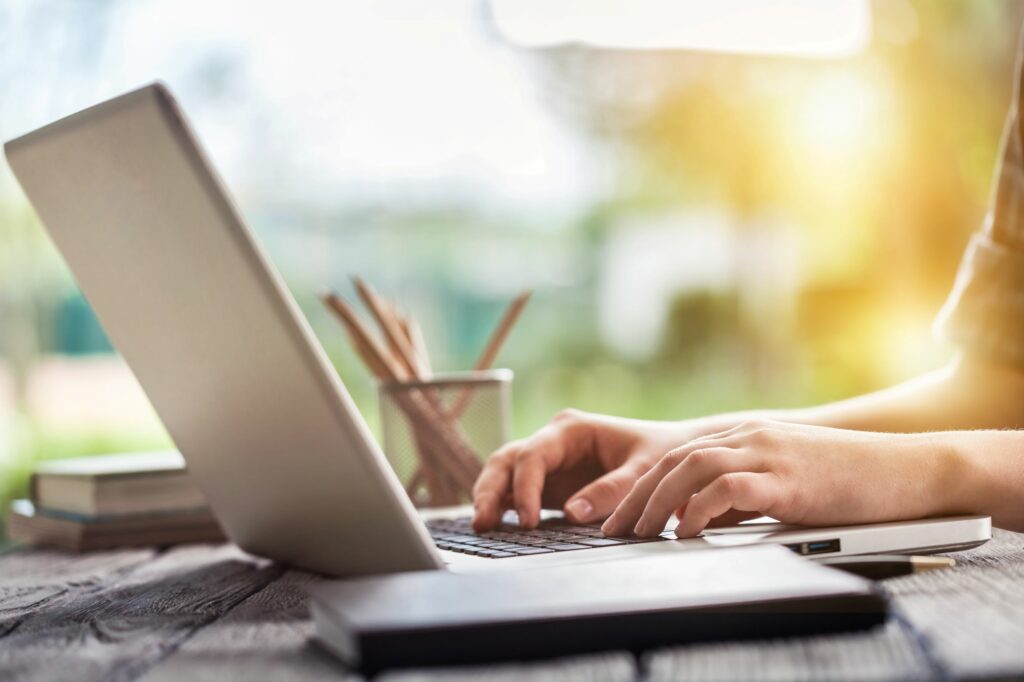 Person writing at their computer on a desk.