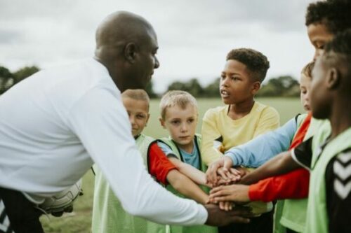 Coach in a huddle with a group of kids preparing for a game.