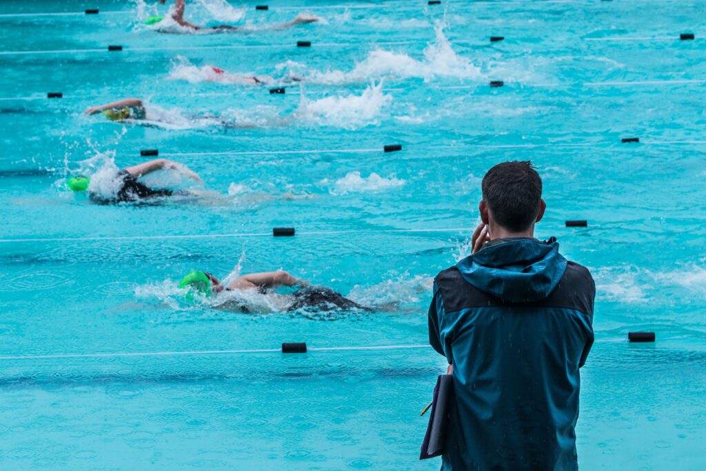 Swimming coach standing on the pool deck watching a group of swimmers racing down their lanes.